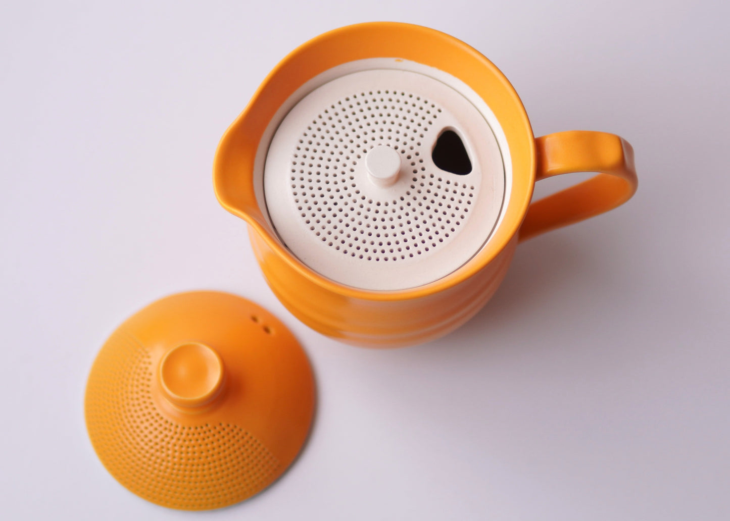 Orange teapot with white interior on a light gray background