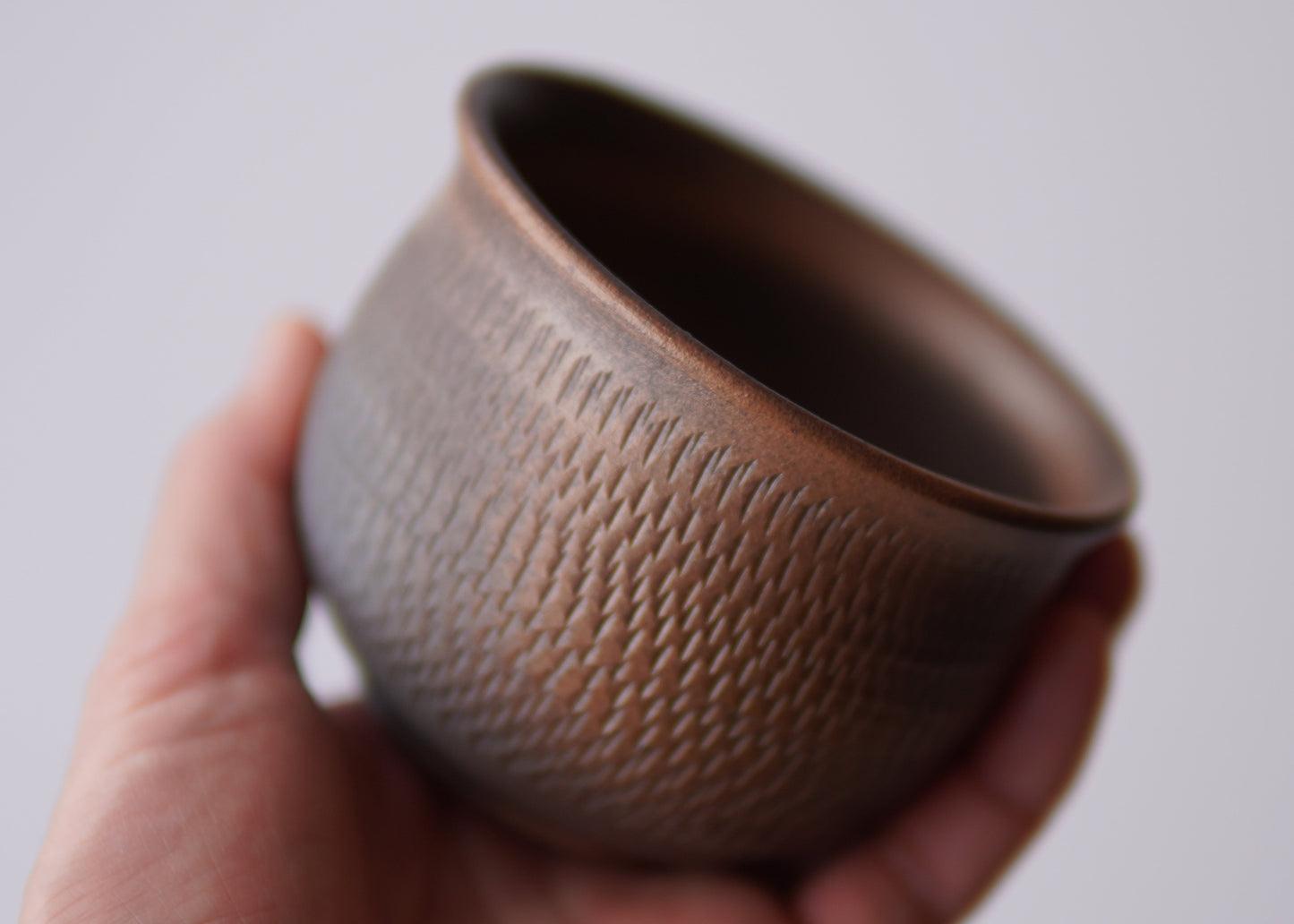 Hand holding a textured brown ceramic cup against a plain background