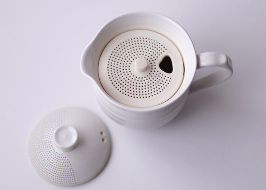 White ceramic teapot with lid on a light gray background