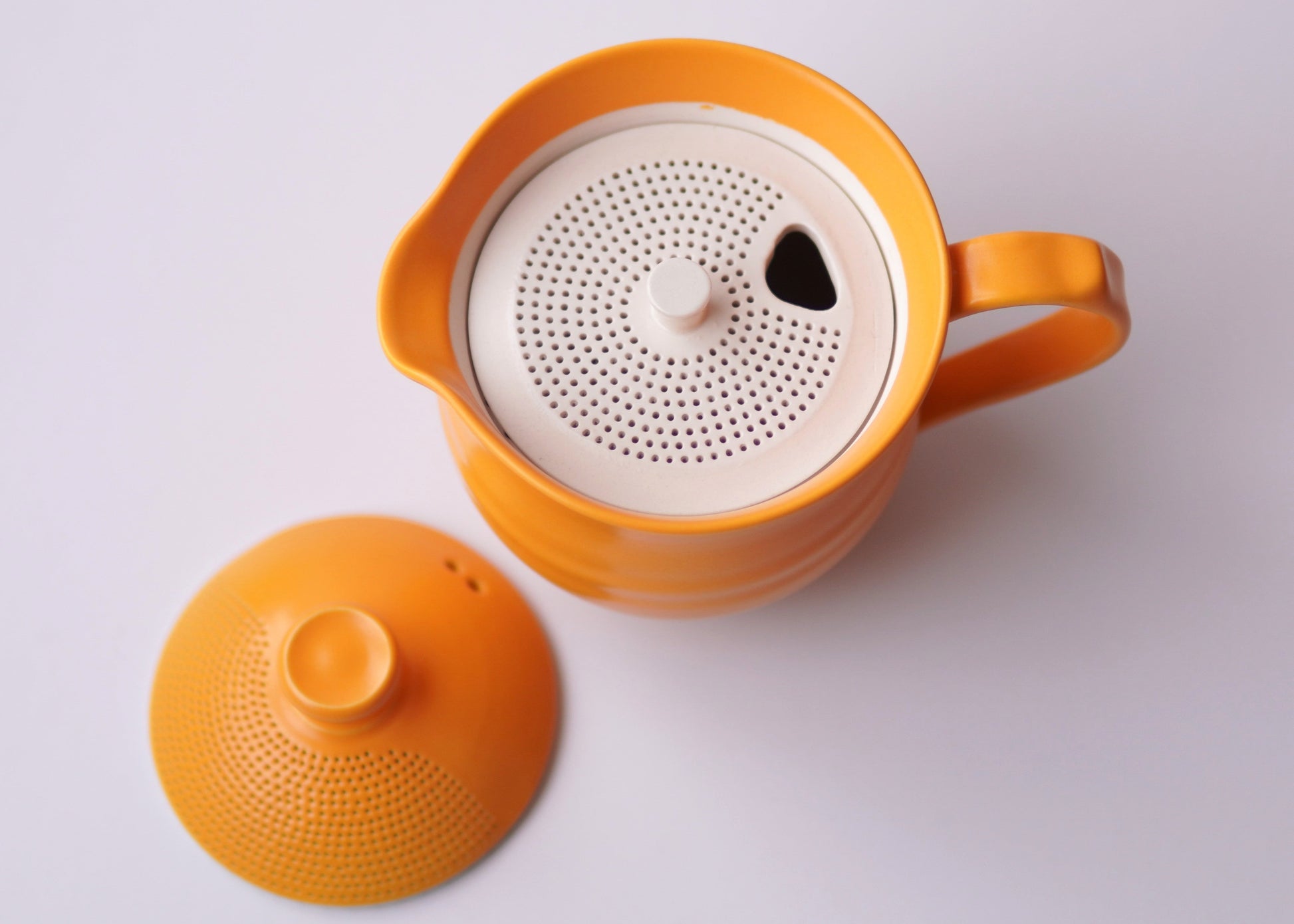 Orange teapot with white interior on a light gray background