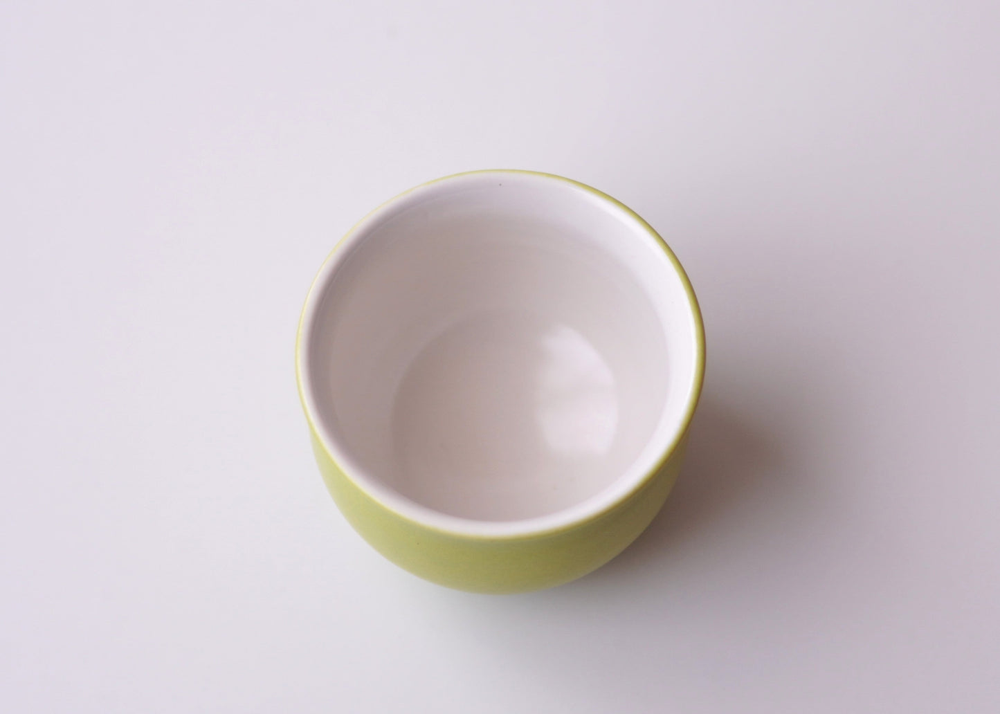 Small white teacup with green rim on a light gray background