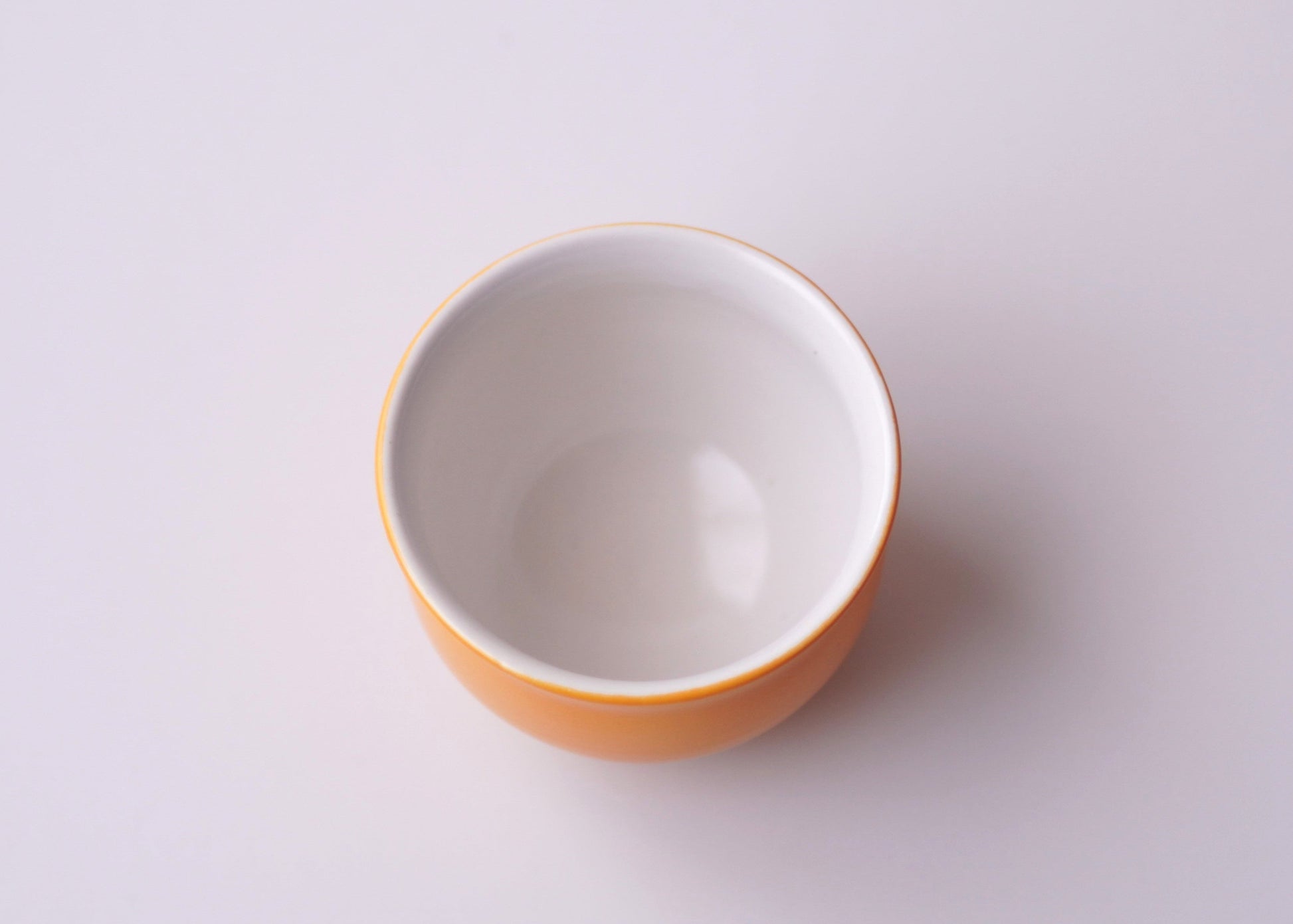 Small white teacup with orange rim on a light gray background